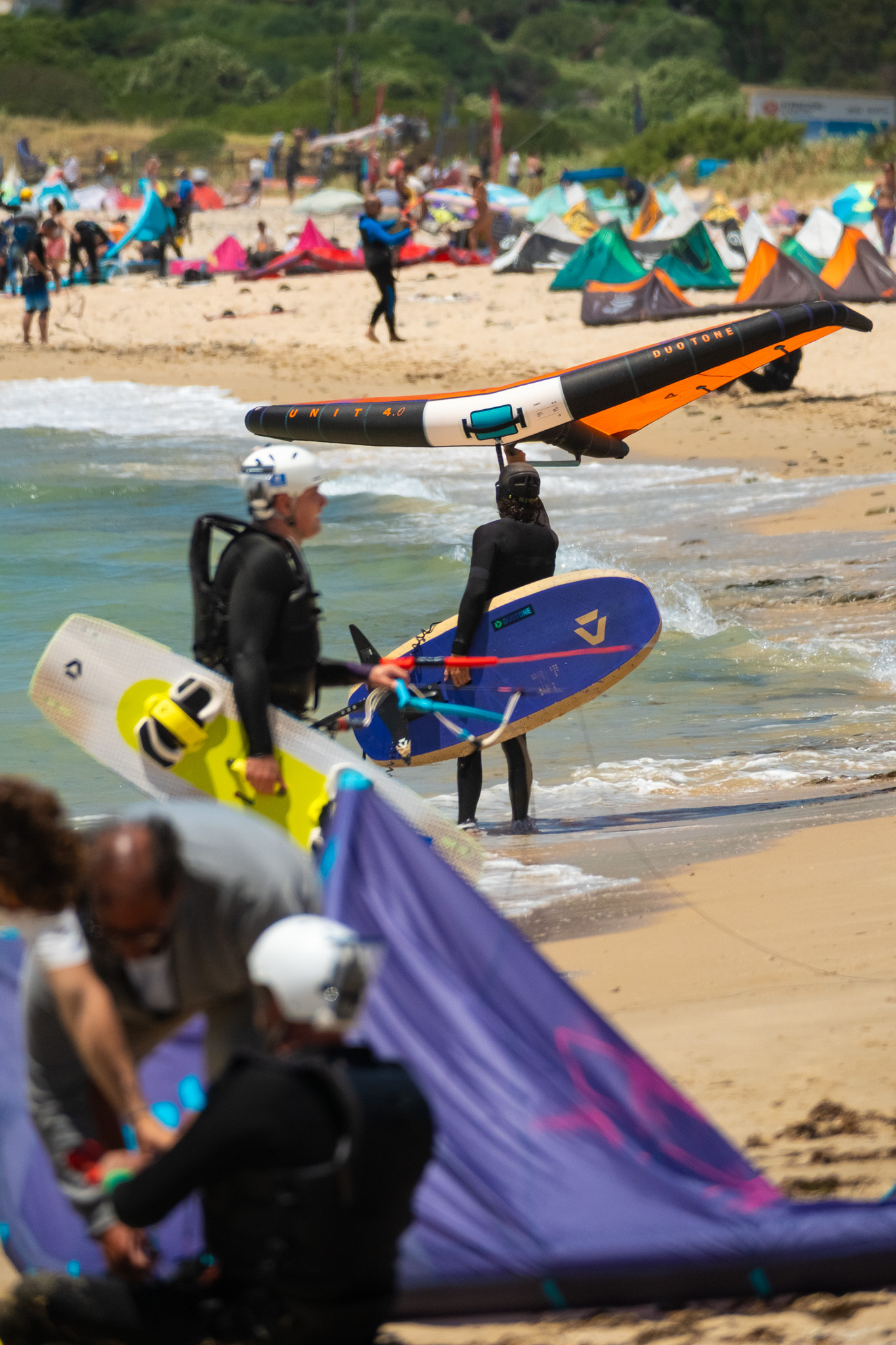 Beginner wingfoil riders carrying boards and wings into the water at Valdevaqueros Beach in Tarifa.