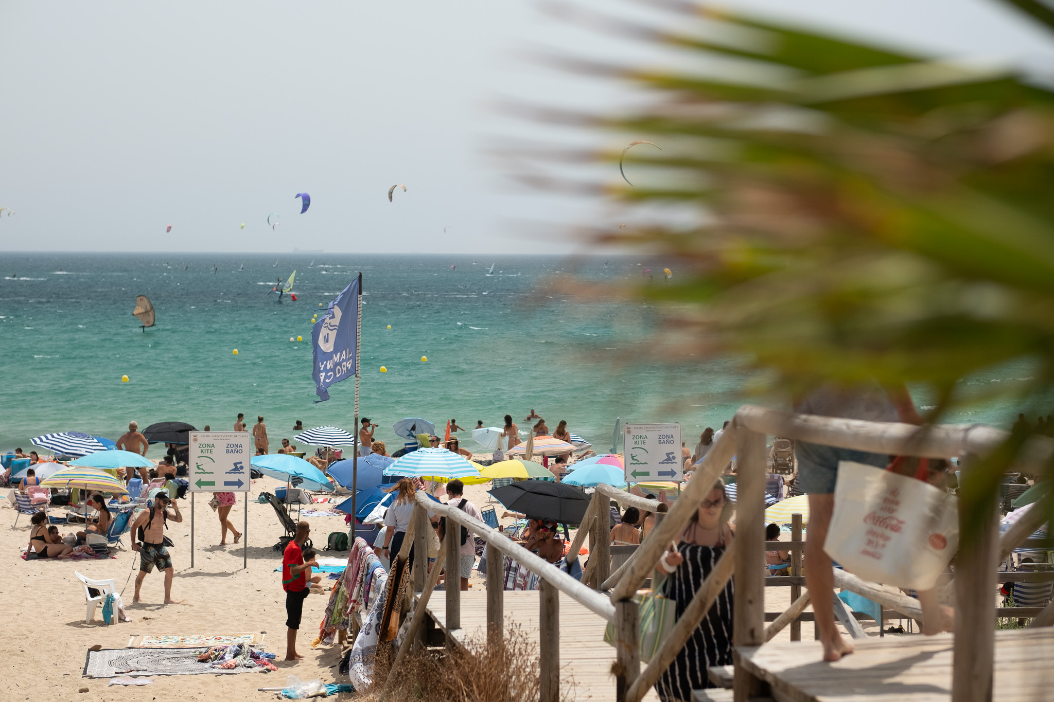 Busy summer day at Valdevaqueros Beach in Tarifa, with beachgoers, umbrellas and kitesurfers on the water during peak season.