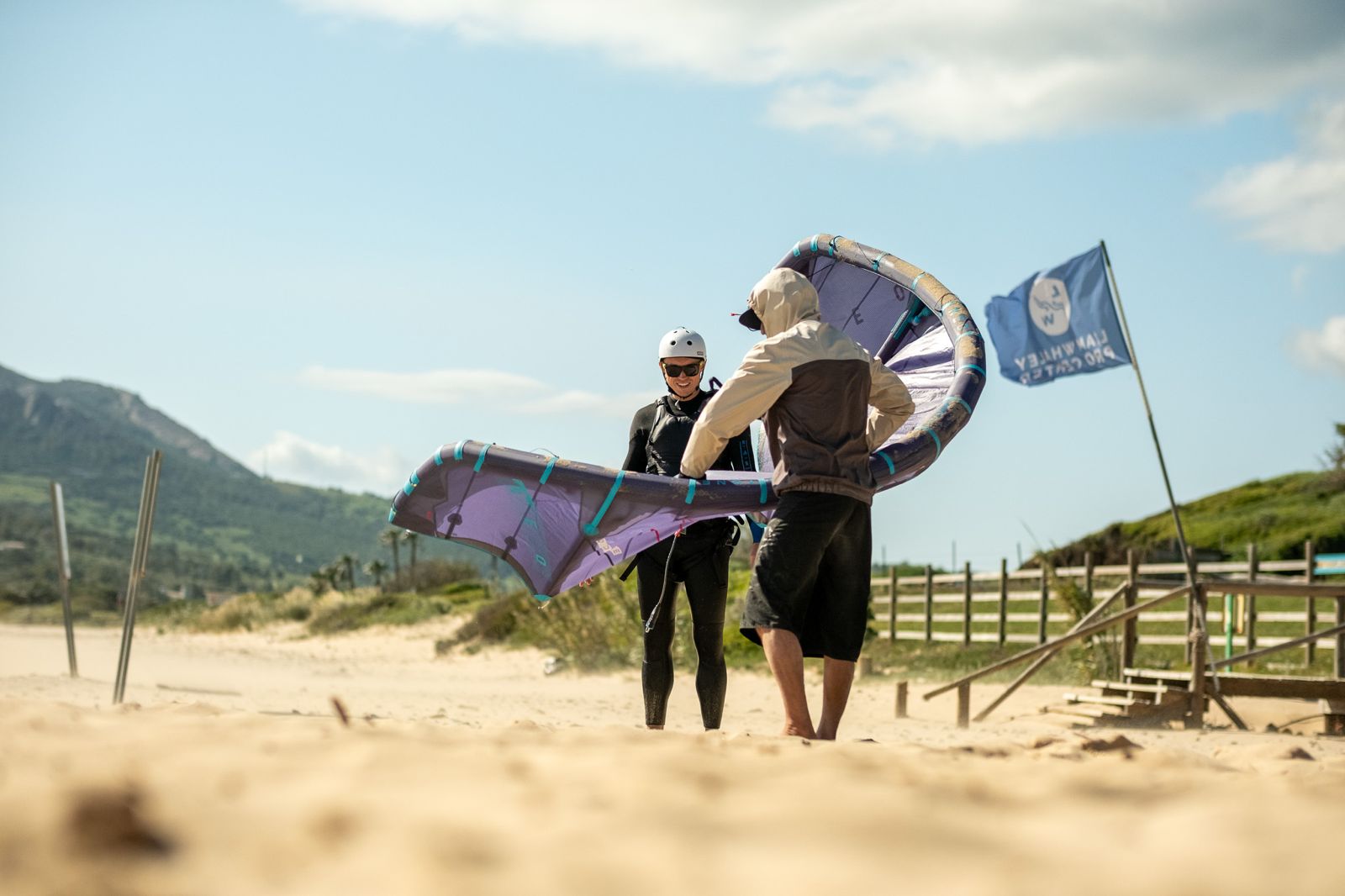Instructor preparing a beginner for a kitesurfing lesson at Valdevaqueros Beach in Tarifa with training kite and safety equipment.