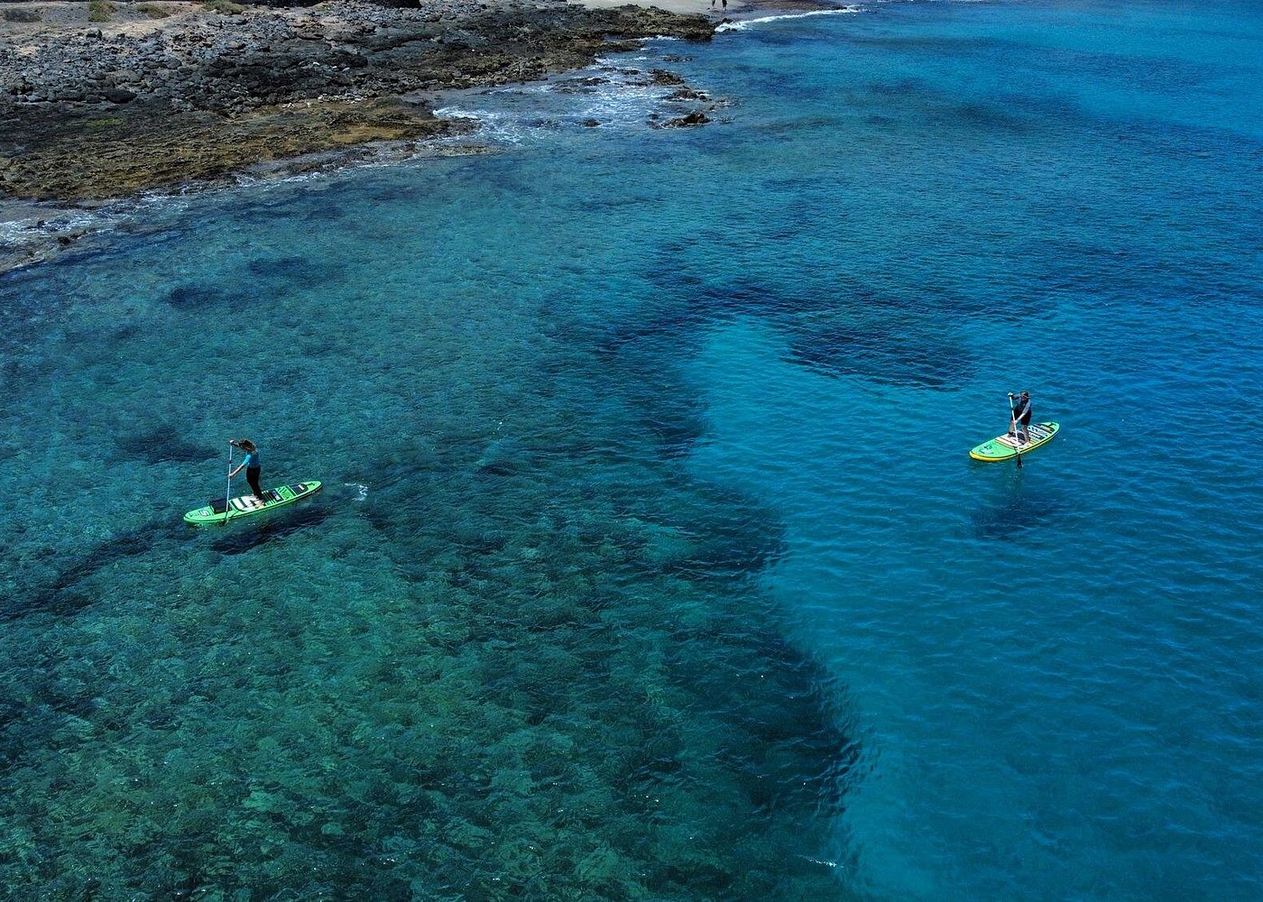Two people paddleboarding in clear turquoise water near the Tarifa coastline on a calm no-wind day