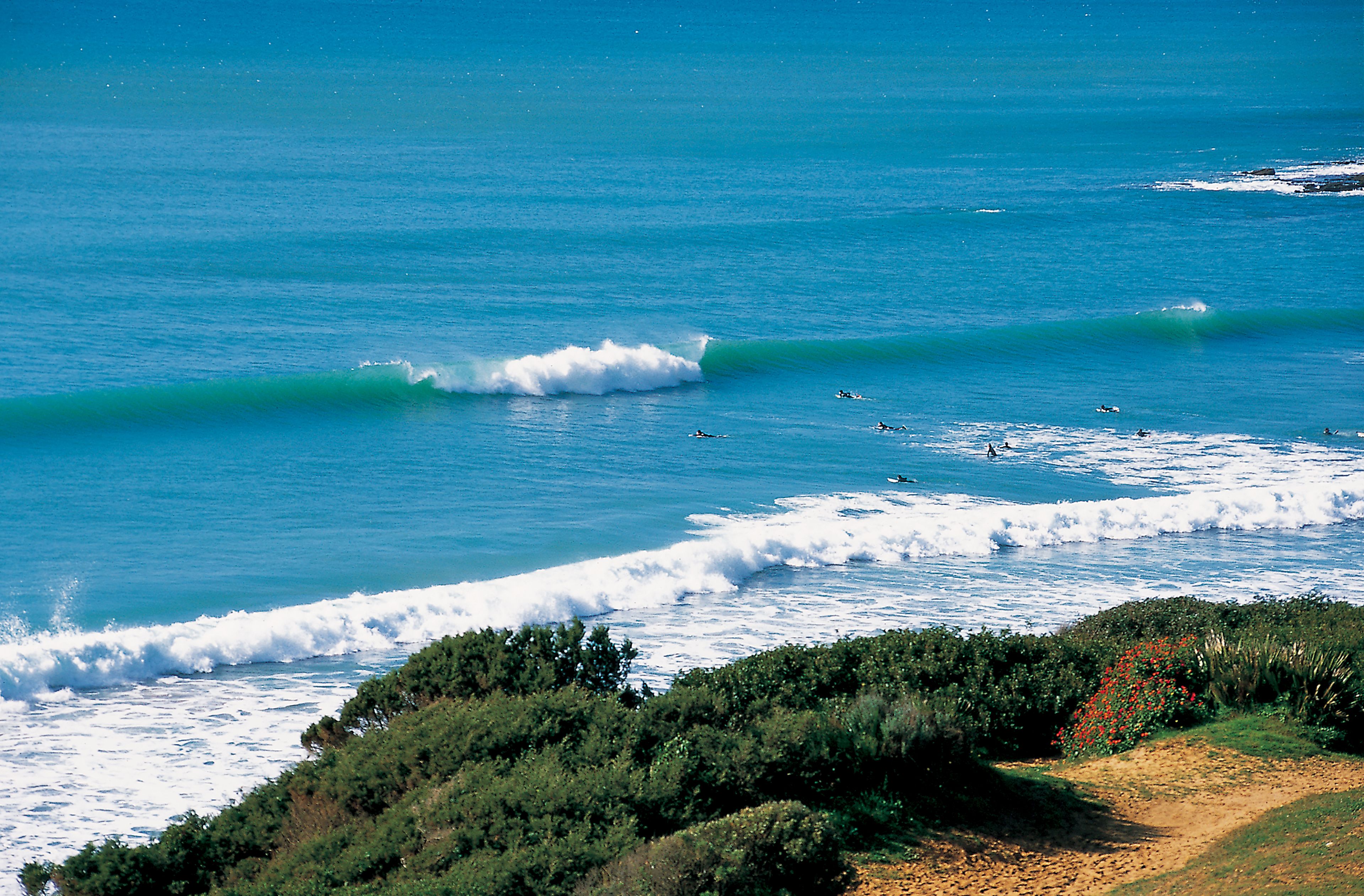 Waves breaking at Los Lances Beach in Tarifa with surfers in the water and coastline views from above