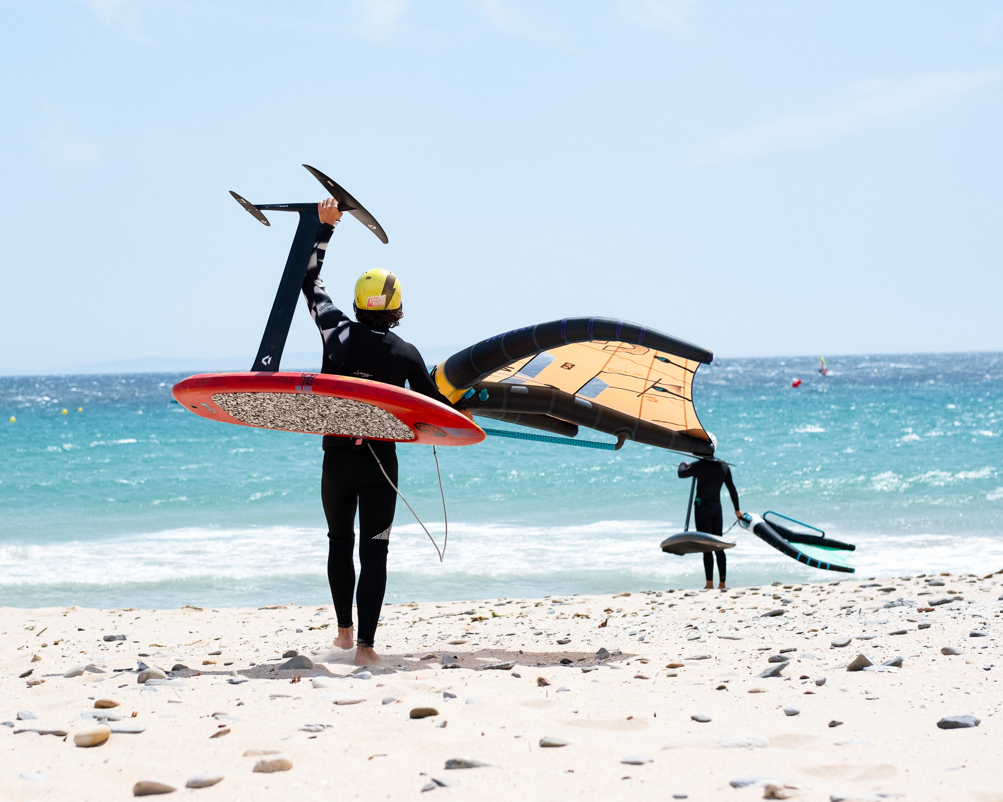 Wingfoil rider carrying a board, foil and wing at Valdevaqueros Beach in Tarifa.